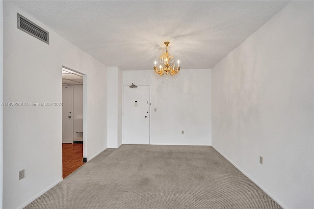 unfurnished room with carpet, a textured ceiling, and a chandelier