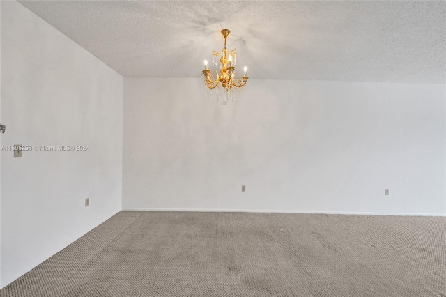 carpeted spare room featuring a textured ceiling and an inviting chandelier