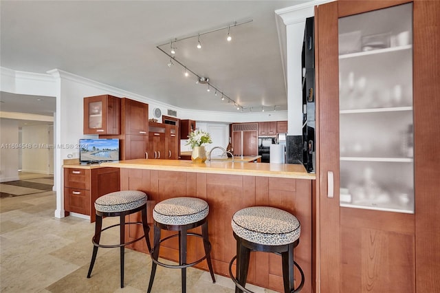 kitchen featuring rail lighting, backsplash, kitchen peninsula, crown molding, and a breakfast bar