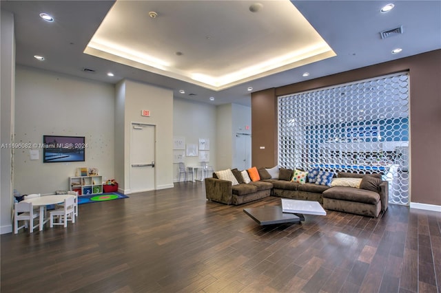 living room with a raised ceiling and dark wood-type flooring