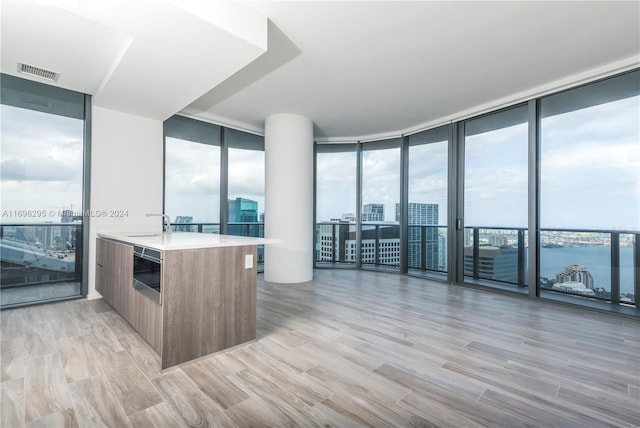 kitchen with kitchen peninsula, a water view, light hardwood / wood-style flooring, and expansive windows