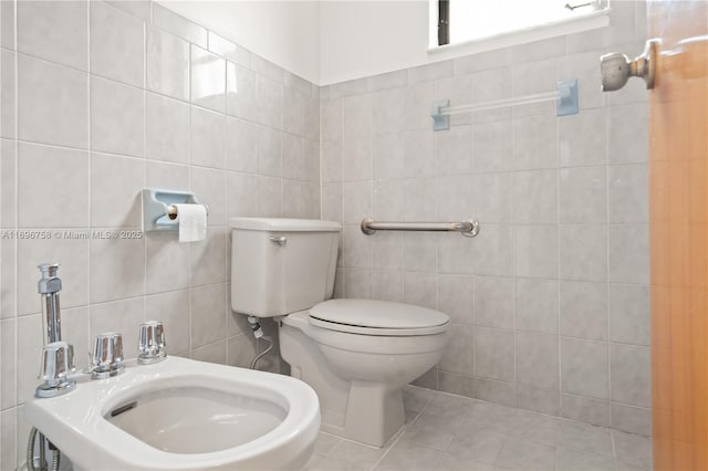 bathroom with a bidet, toilet, tile patterned flooring, and tile walls