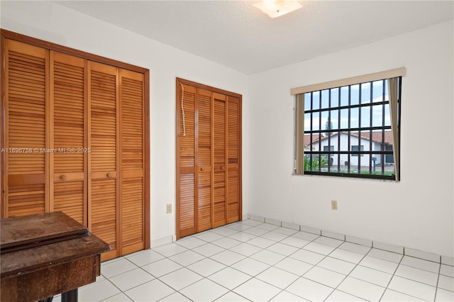 bedroom featuring multiple closets, light tile patterned flooring, and a textured ceiling