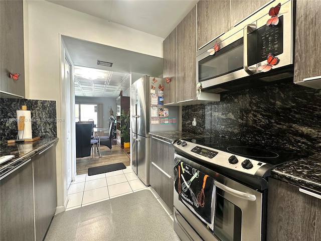 kitchen featuring backsplash, dark stone countertops, light tile patterned floors, appliances with stainless steel finishes, and dark brown cabinetry