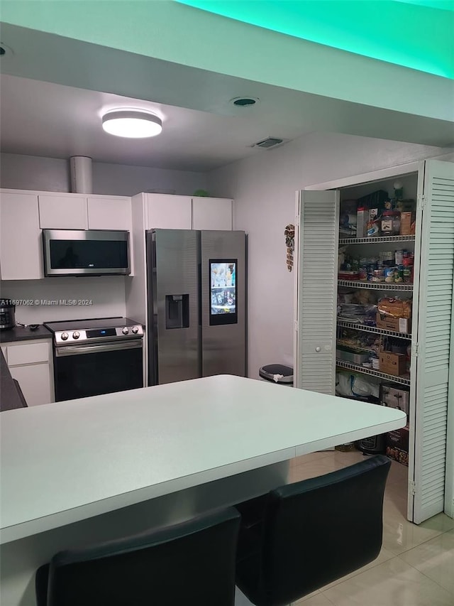 kitchen with white cabinets, stainless steel appliances, and light tile patterned flooring