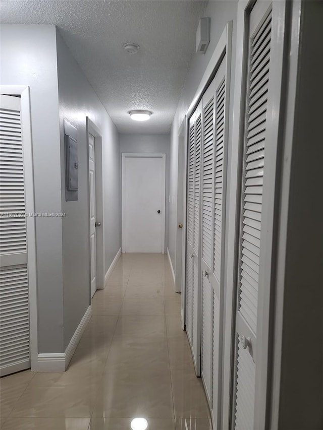 corridor featuring light tile patterned floors, a textured ceiling, and electric panel