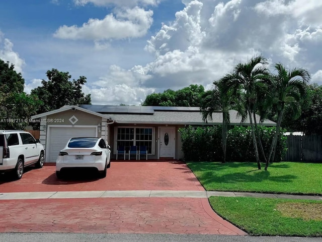 ranch-style home with fence, a front lawn, a garage, decorative driveway, and roof mounted solar panels