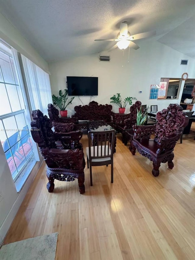 living area with ceiling fan, lofted ceiling, wood-type flooring, and a textured ceiling