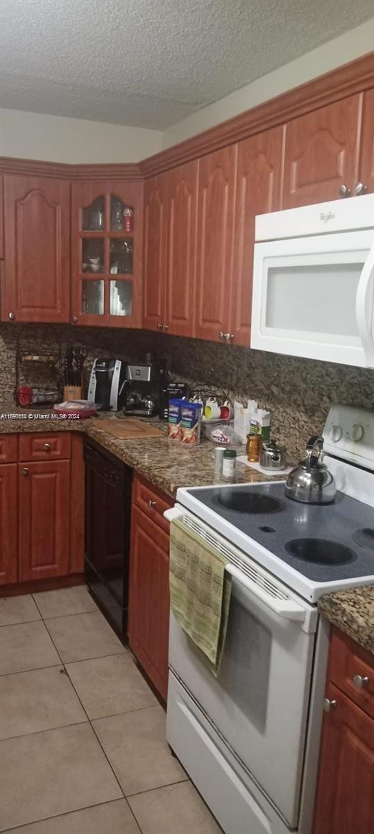 kitchen with decorative backsplash, dark stone counters, white appliances, a textured ceiling, and light tile patterned floors