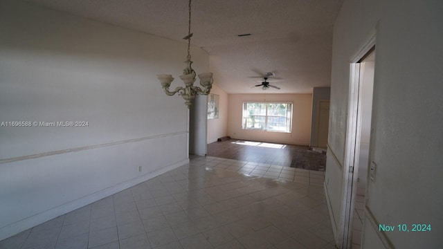 tiled spare room featuring ceiling fan with notable chandelier, a textured ceiling, and vaulted ceiling