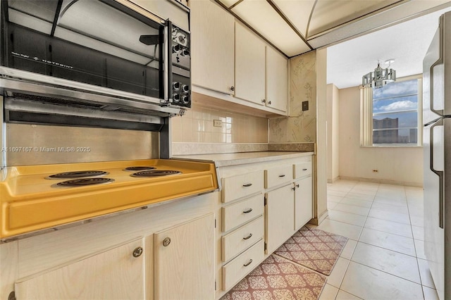 kitchen with light tile patterned flooring, refrigerator, tasteful backsplash, stovetop, and a notable chandelier