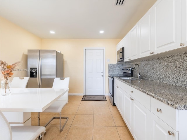 kitchen featuring appliances with stainless steel finishes, dark stone counters, sink, white cabinets, and light tile patterned flooring