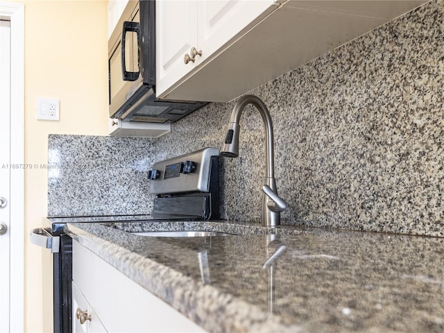 kitchen featuring tasteful backsplash, white cabinetry, and dark stone countertops