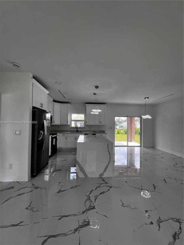 kitchen featuring light stone countertops, black fridge with ice dispenser, sink, decorative light fixtures, and white cabinetry