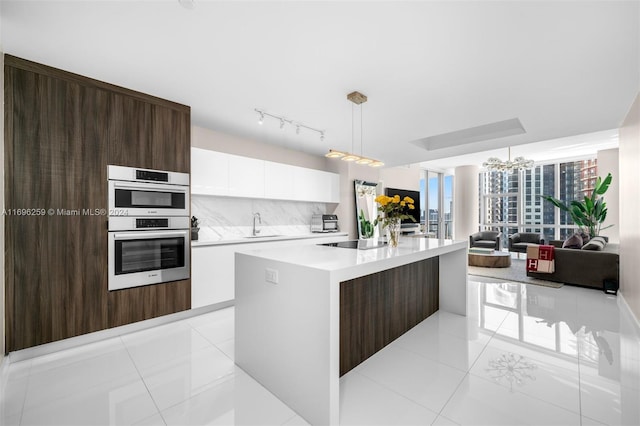 kitchen with decorative backsplash, double oven, decorative light fixtures, white cabinets, and an island with sink