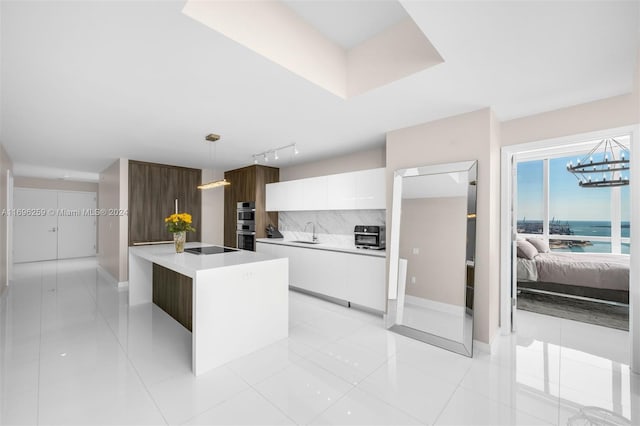 kitchen featuring a water view, sink, light tile patterned floors, decorative light fixtures, and white cabinetry