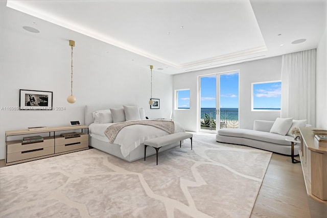 bedroom featuring a water view, light hardwood / wood-style flooring, access to outside, and a tray ceiling