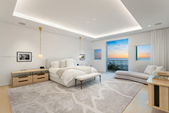 bedroom with wood-type flooring, access to outside, and a tray ceiling