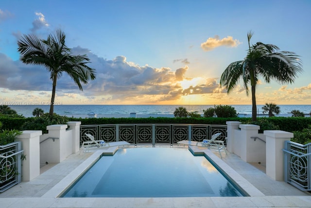 pool at dusk featuring a water view and a hot tub