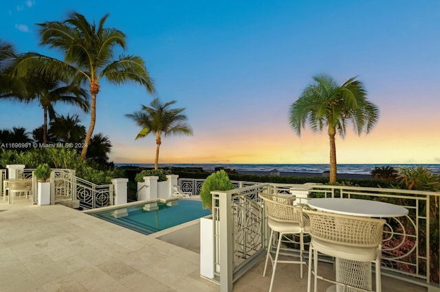 pool at dusk with a patio and a water view