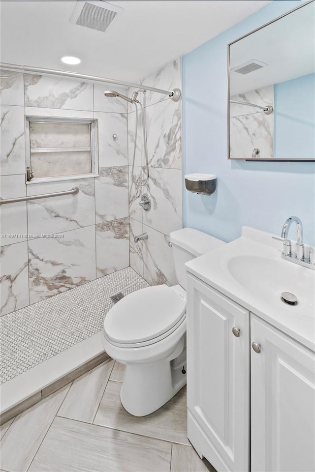 bathroom with a tile shower, vanity, and toilet