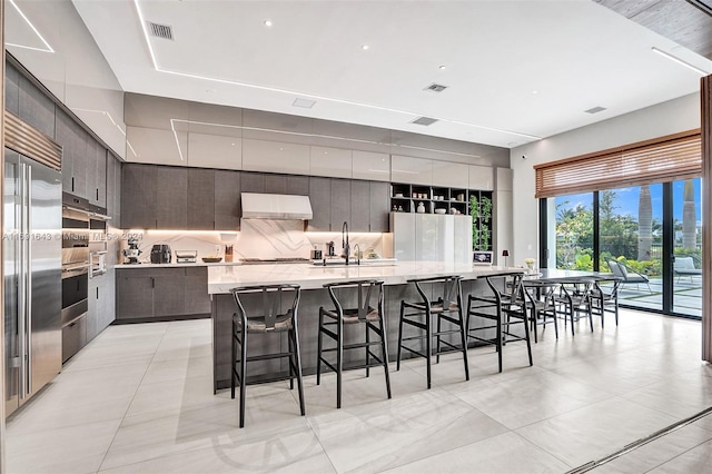 kitchen with decorative backsplash, a breakfast bar, sink, exhaust hood, and a large island