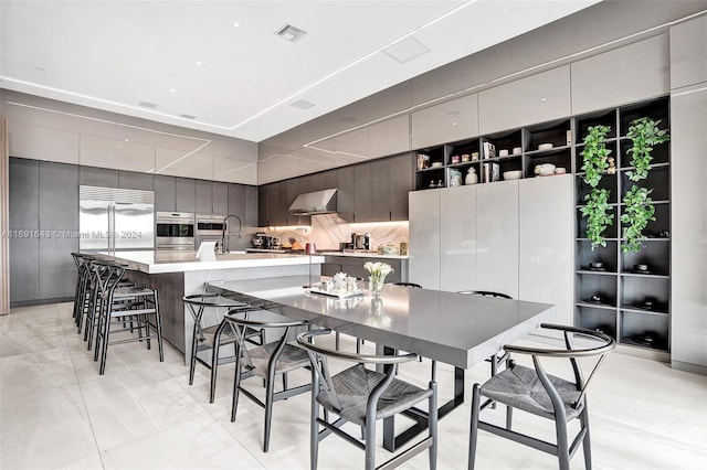 kitchen featuring a large island, wall chimney range hood, tasteful backsplash, a kitchen breakfast bar, and stainless steel built in fridge