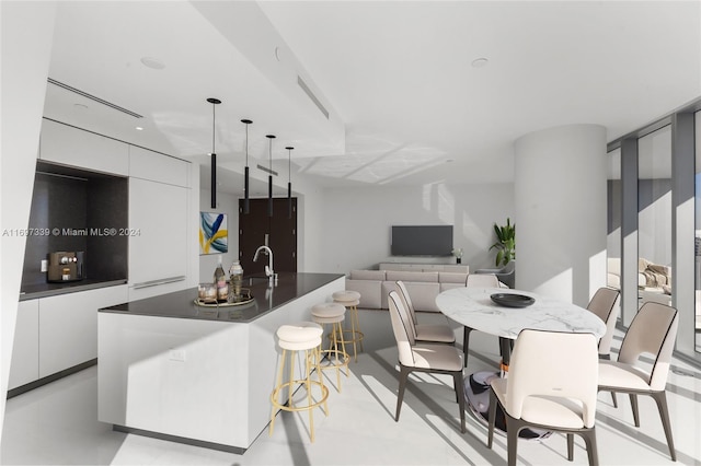 kitchen with white cabinetry, sink, decorative light fixtures, a breakfast bar area, and a center island with sink