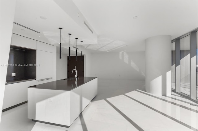 kitchen featuring white cabinets, pendant lighting, an island with sink, and sink