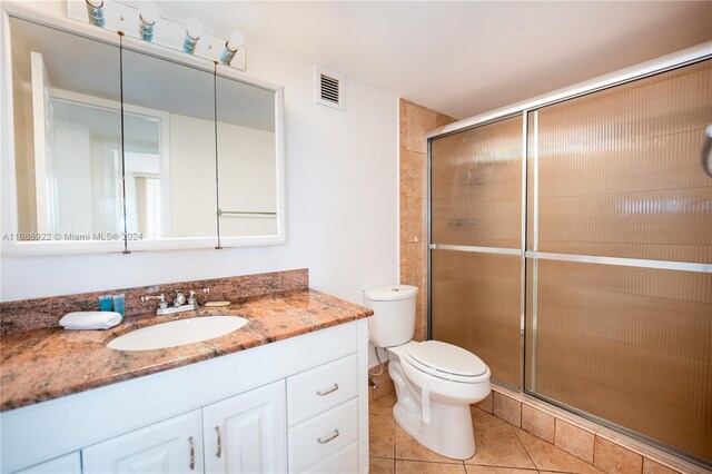 bathroom with tile patterned flooring, vanity, toilet, and an enclosed shower