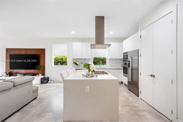 kitchen with white cabinets, decorative backsplash, island range hood, and stainless steel appliances