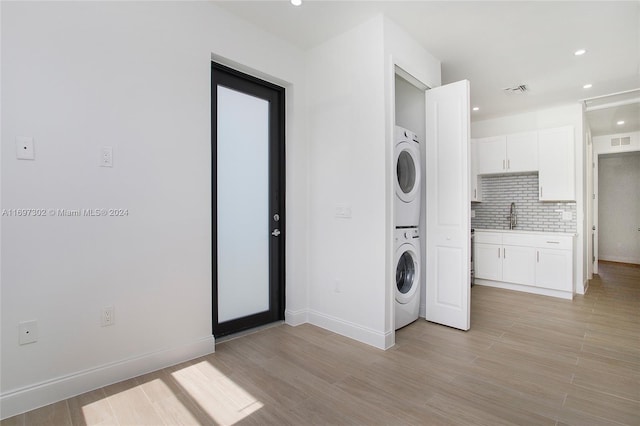 laundry area with light hardwood / wood-style floors, stacked washer / dryer, and sink