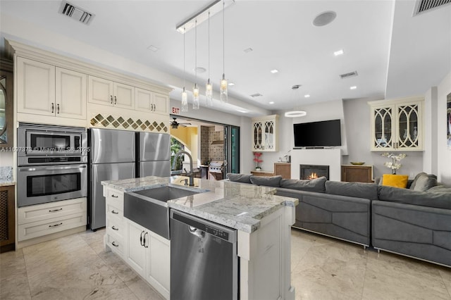 kitchen featuring sink, appliances with stainless steel finishes, cream cabinets, an island with sink, and decorative light fixtures