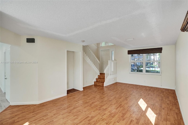 unfurnished living room with a textured ceiling and light hardwood / wood-style floors