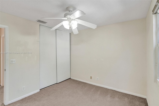 unfurnished bedroom with a closet, a textured ceiling, light colored carpet, and ceiling fan