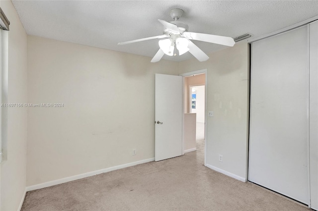 unfurnished bedroom featuring ceiling fan, a textured ceiling, light carpet, and a closet