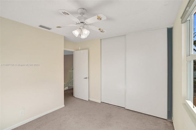 unfurnished bedroom with multiple windows, light colored carpet, a closet, and ceiling fan