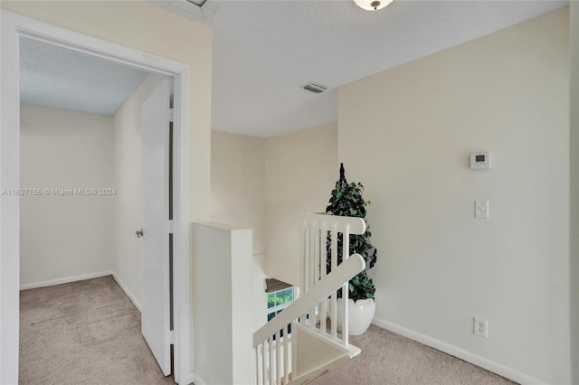 hallway featuring light colored carpet and a textured ceiling