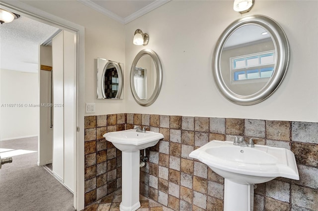 bathroom featuring a textured ceiling, dual sinks, crown molding, and tile walls