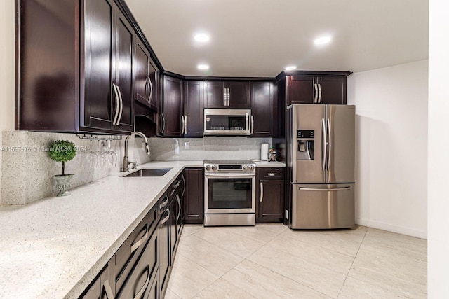 kitchen with decorative backsplash, appliances with stainless steel finishes, light stone counters, dark brown cabinets, and sink