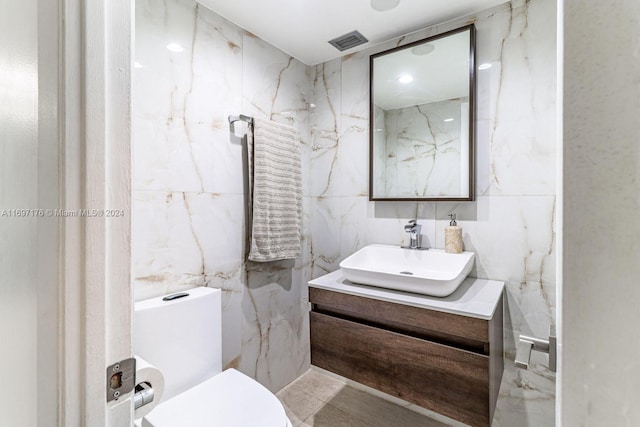 bathroom featuring vanity, toilet, and tile walls