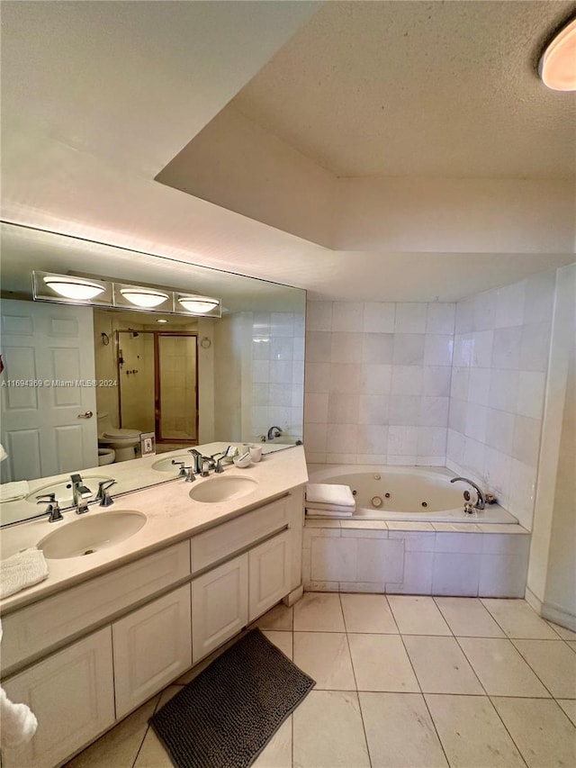 bathroom with a textured ceiling, vanity, a relaxing tiled tub, tile patterned flooring, and toilet