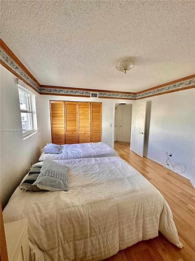 bedroom with crown molding, hardwood / wood-style floors, and a textured ceiling