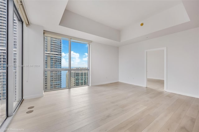 empty room with a water view, a raised ceiling, and light hardwood / wood-style floors