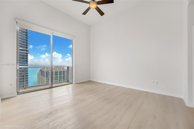 empty room featuring ceiling fan, a healthy amount of sunlight, a water view, and light hardwood / wood-style flooring