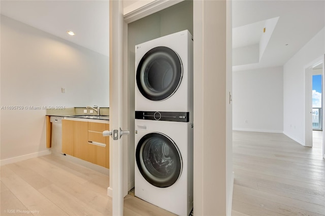 clothes washing area featuring light hardwood / wood-style flooring, stacked washer / dryer, and sink