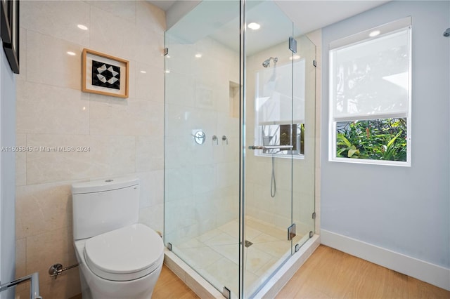 bathroom featuring hardwood / wood-style floors, toilet, tile walls, and a shower with shower door