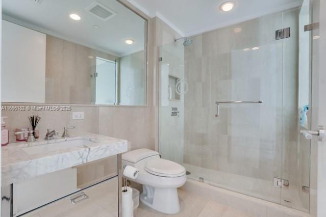 bathroom featuring toilet, decorative backsplash, vanity, a shower with shower door, and tile walls