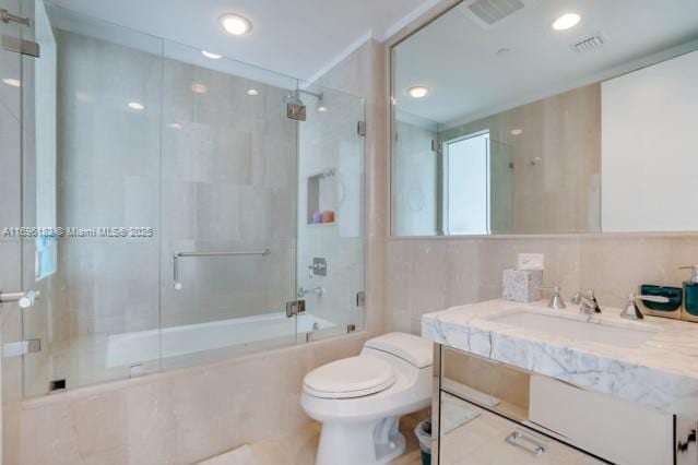 full bathroom featuring shower / bath combination with glass door, vanity, tile walls, and toilet