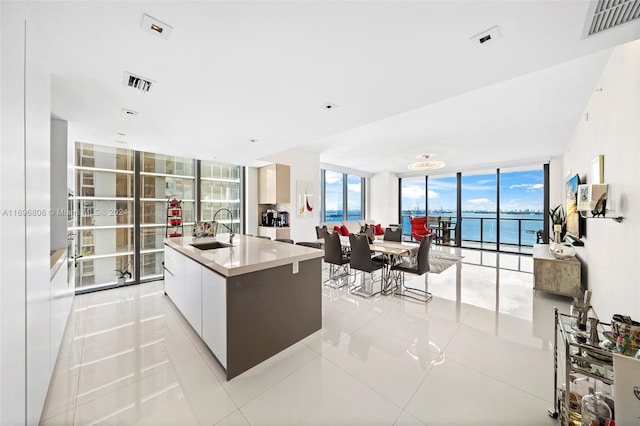 kitchen featuring white cabinetry, sink, light tile patterned floors, a center island with sink, and a water view